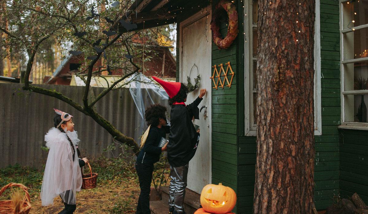 three kids outside the door of the house trick-or-treating
