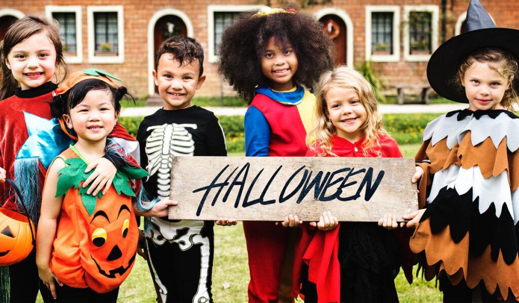 six kids wearing Halloween costumes holding a halloween sign