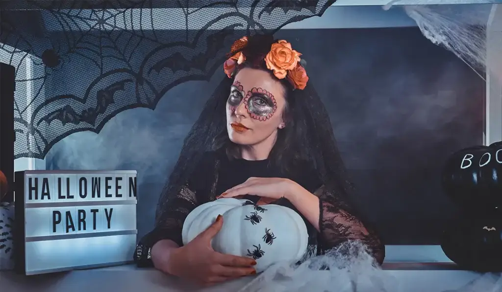 Spooky Virtual Halloween scene with woman in makeup, white pumpkin with spiders, and Halloween Party sign.